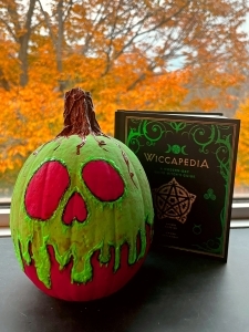 pumpkin painted red & green with ghoulish eyes & book behind it