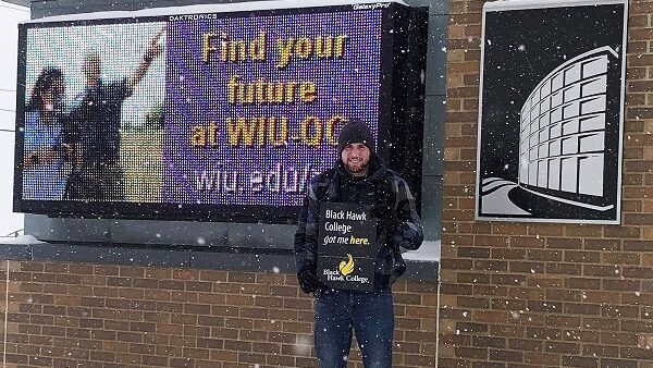 student holds BHC sign in front of Western Illinois University signage