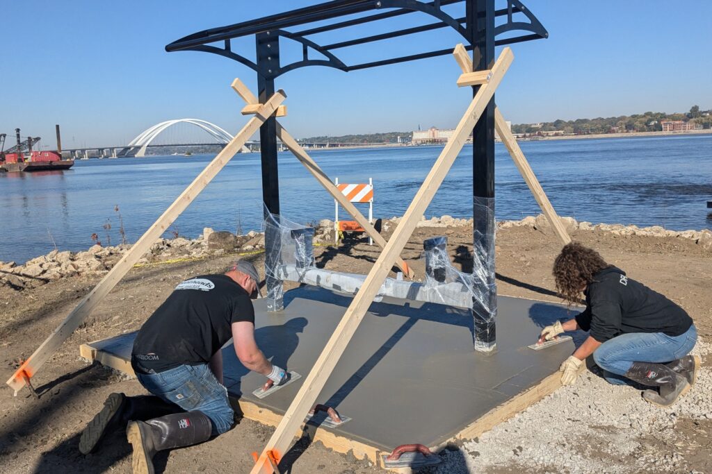 2 people smoothing out concrete pad at picnic table shelter