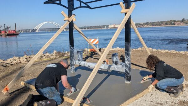 2 people smoothing out concrete pad at picnic table shelter