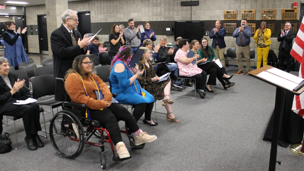 smiling students seated with audience standing and clapping