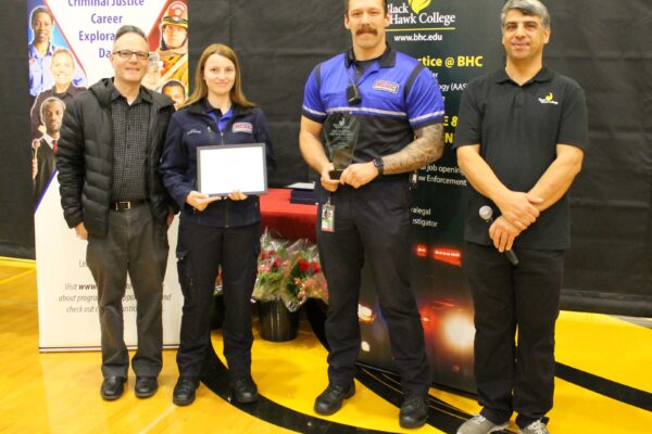 4 people standing in front of pull-up banners and one holding award certificate 