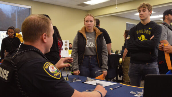 Two students chat with a uniformed man at a table.