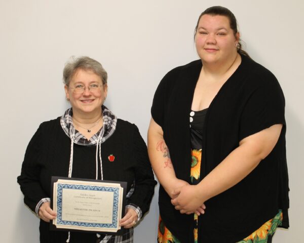 2 people standing against wall with one person holding a certificate