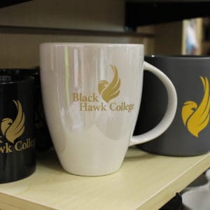 White coffee mug with Black Hawk College logo on a store shelf