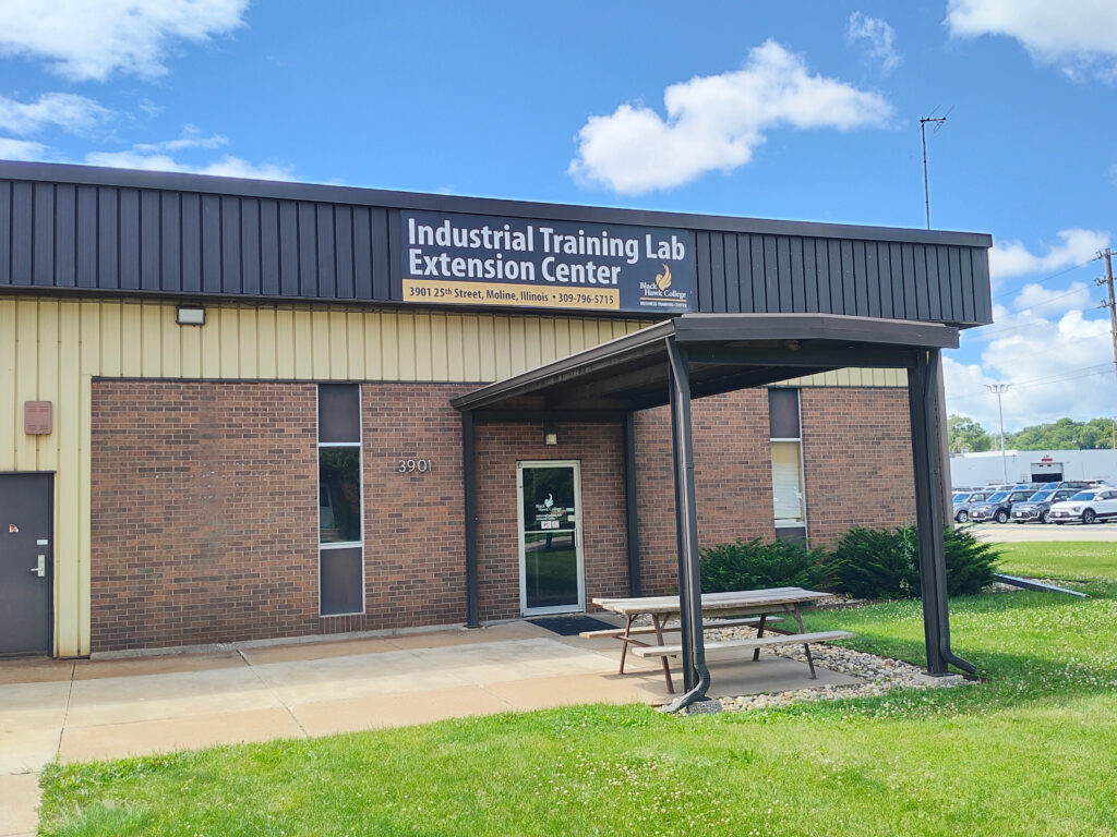 Black Hawk College Industrial Training Lab Extension Center. A brown brick building with black siding with a green lot in front of a blue sky.