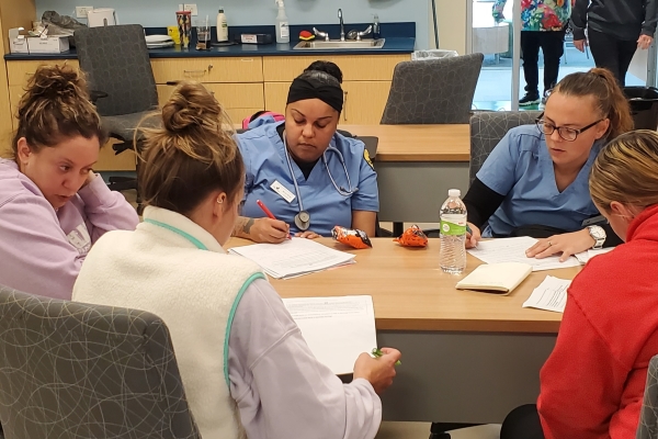 5 people sitting at table taking notes with two wearing scrubs