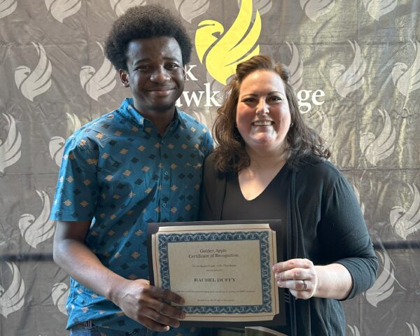 2 people standing in front of backdrop with one person holding a certificate