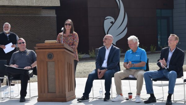 MaryBeth Stopoulos standing at podium outside Building 3 with 4 people seated by podium