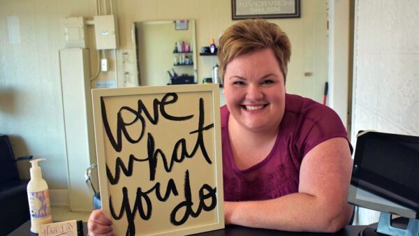 woman leaning on counter holding a sign that reads love what you do