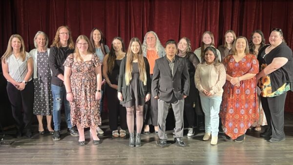 group of 16 people standing on theatre stage