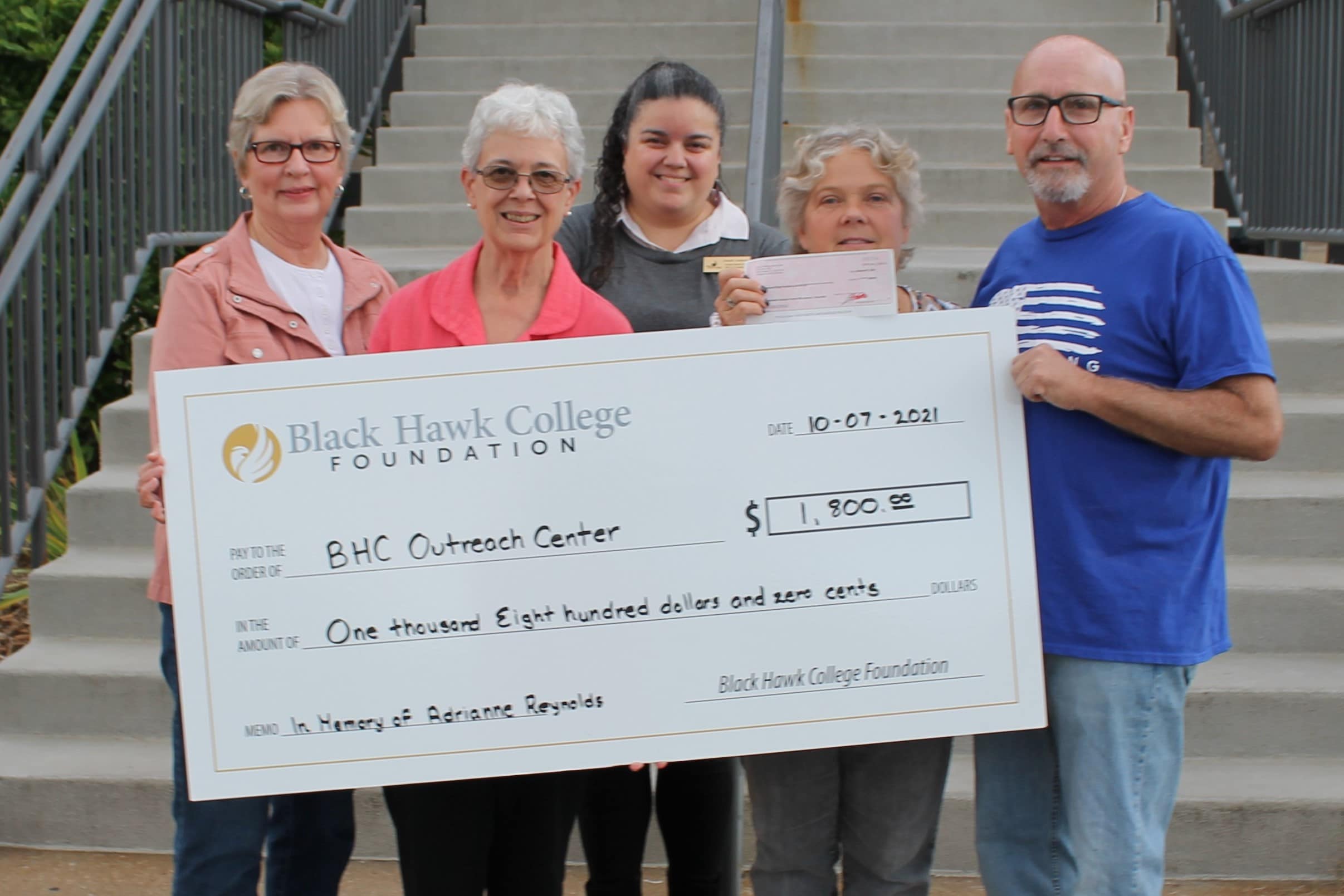 5 people standing outside Outreach Center with oversized check