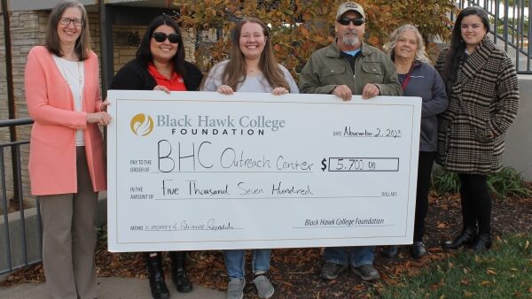 6 people standing outdoors holding oversized check