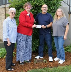 4 people standing outdoors with a check