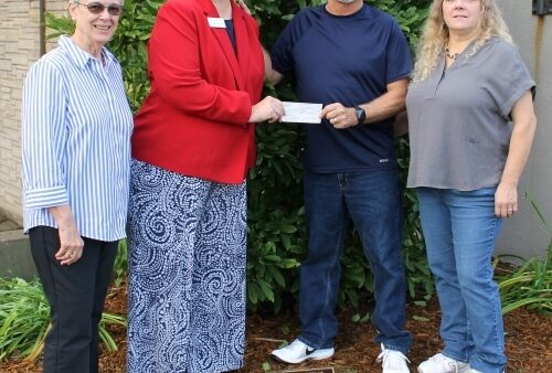 4 people standing outdoors with a check