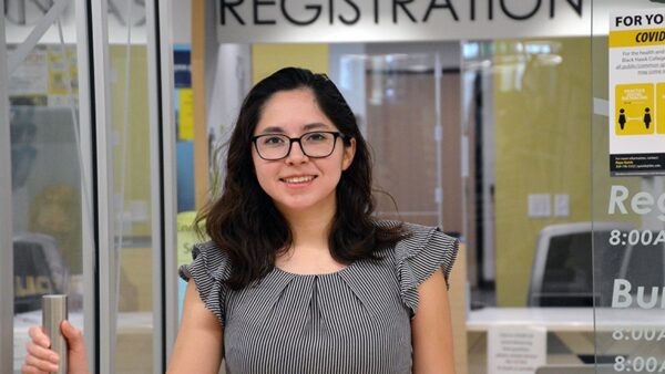 smiling female student holding a door handle with REGISTRATION sign above her