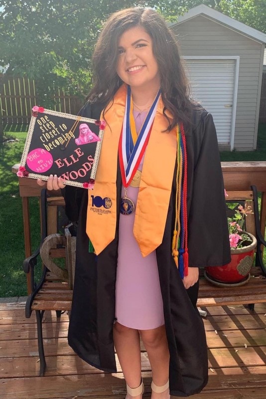 smiling graduate wearing her gown and holding a cap