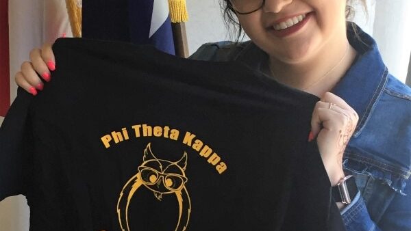 smiling student holding up a Phi Theta Kappa t-shirt