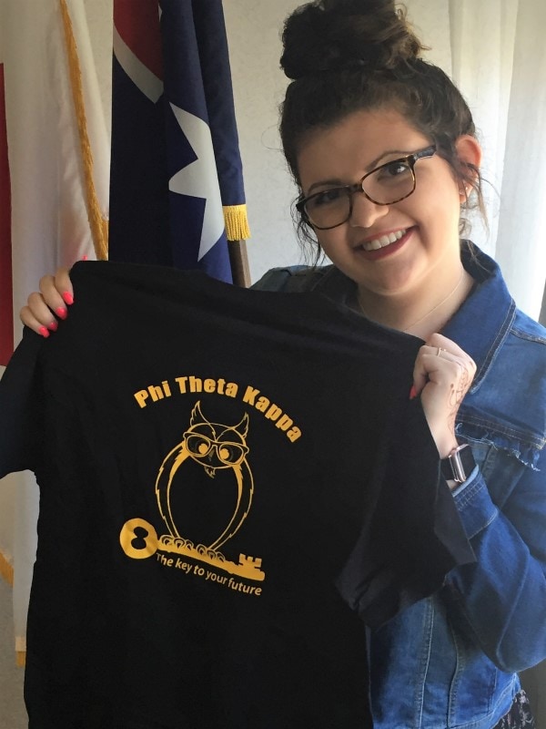 smiling student holding up a Phi Theta Kappa t-shirt