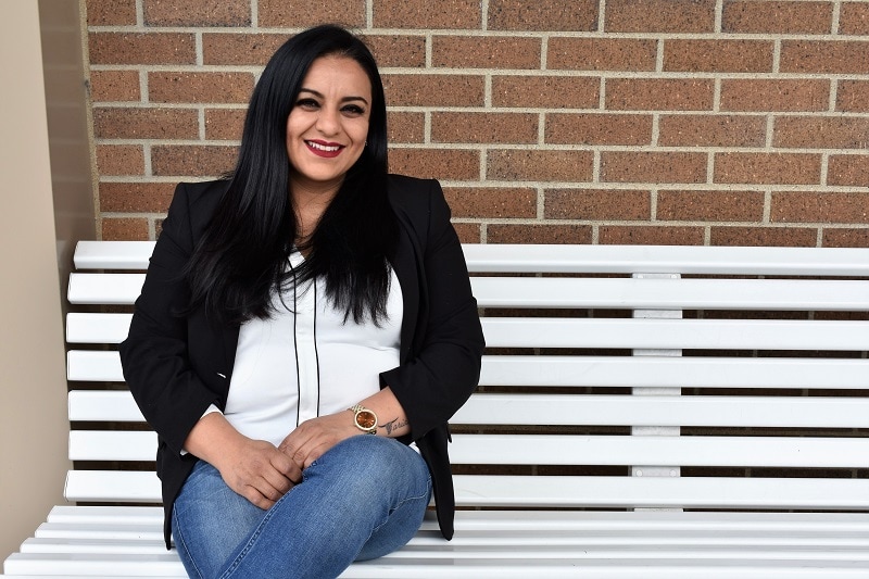 student sitting on a white bench against a brick wall