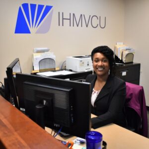 BHC graduate Tamica Reynolds sitting at desk with sign behind her "IHMVCU"