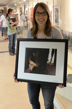 student holding framed art in front of an exhibit