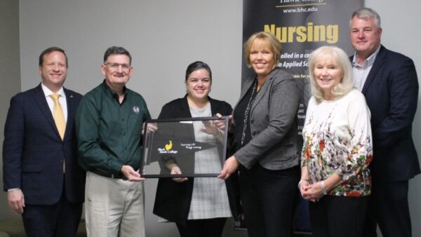 6 people standing in front of nursing banner with framed Black Hawk College pennant