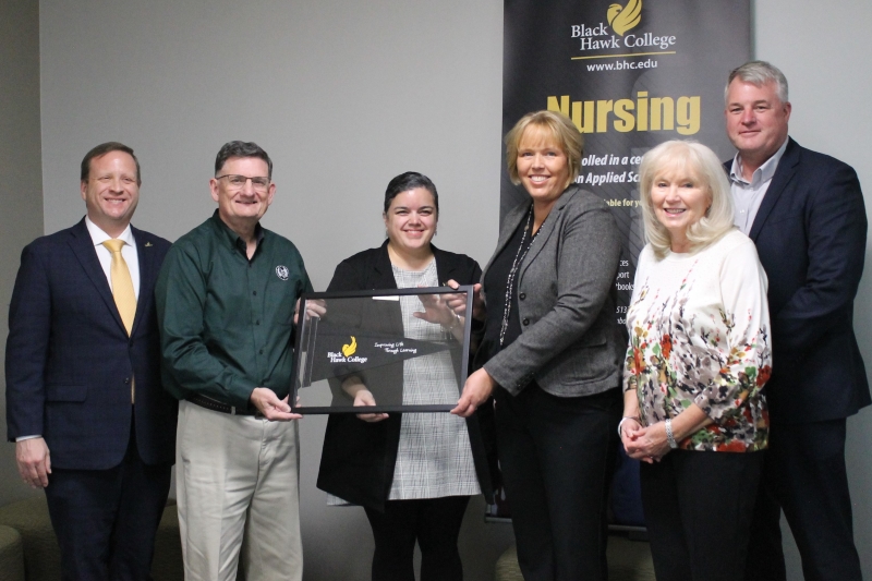 6 people standing in front of nursing banner with framed Black Hawk College pennant