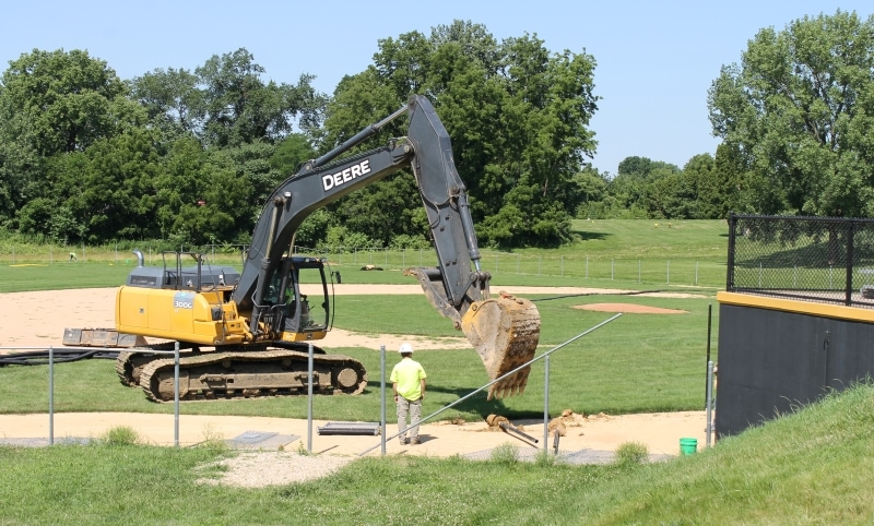 excavator removing fence post at baseball field