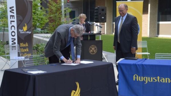 Tim Wynes signing document on table outdoors with 2 people watching and smiling