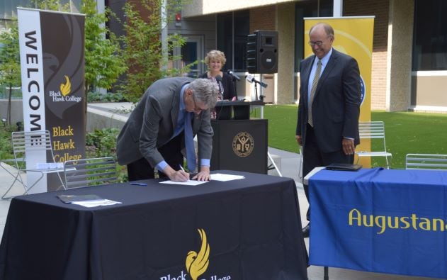 Tim Wynes signing document on table outdoors with 2 people watching and smiling