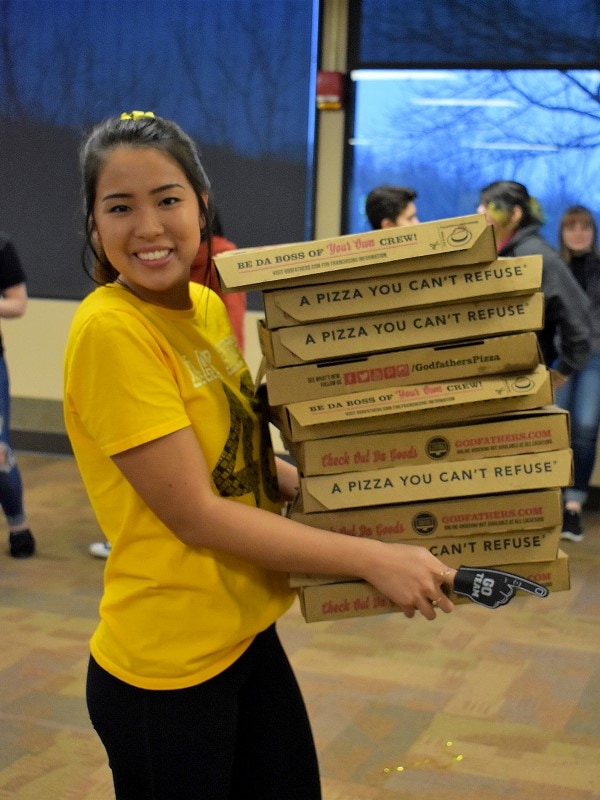 smiling student holding stack of pizza boxes