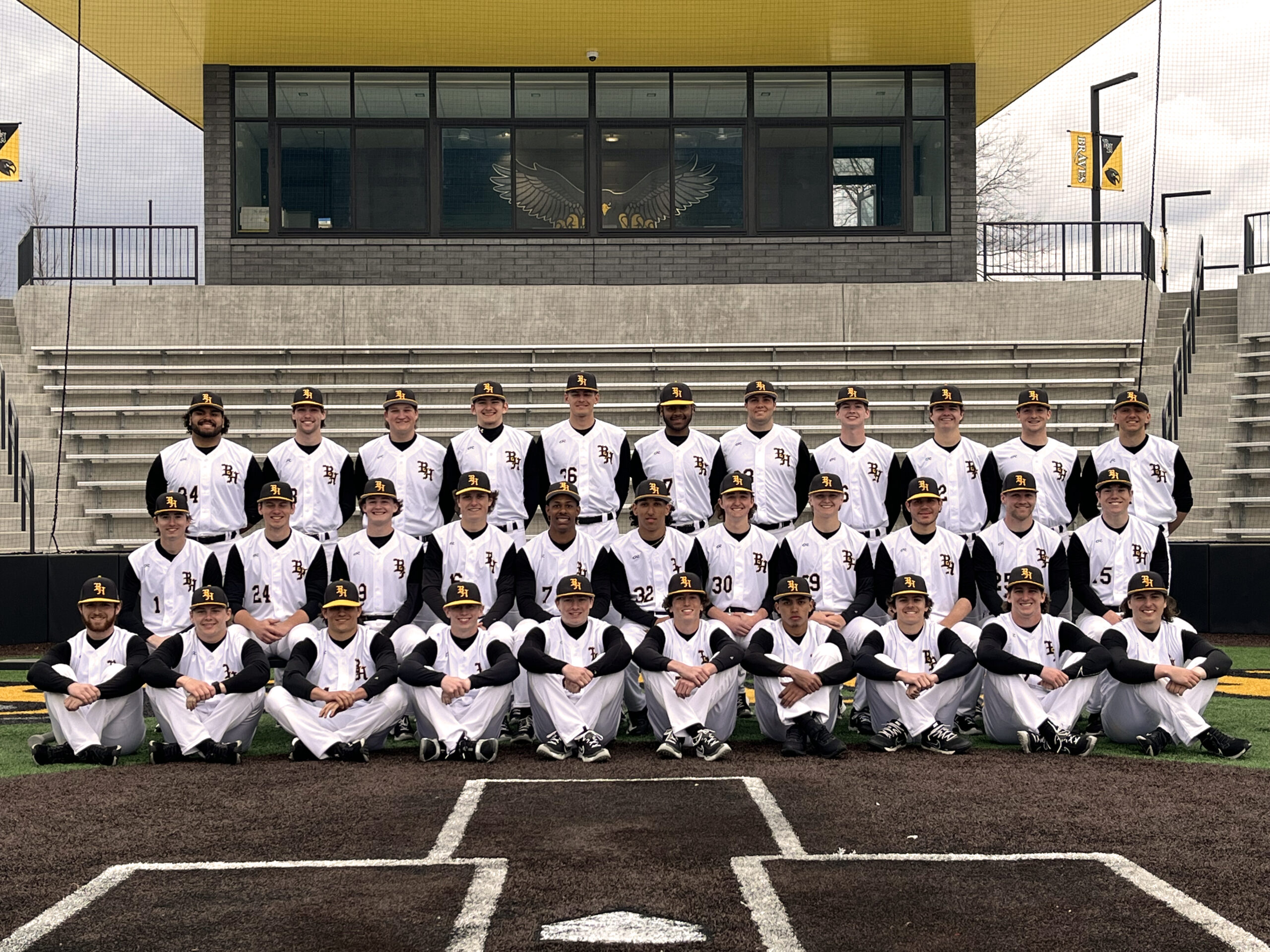 team of baseball players seated and standing at first base on field in new BHC athletic complex