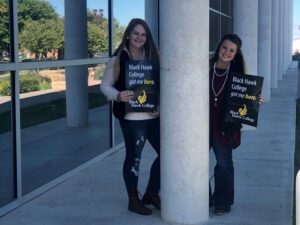 two female college students holding Black Hawk College signs