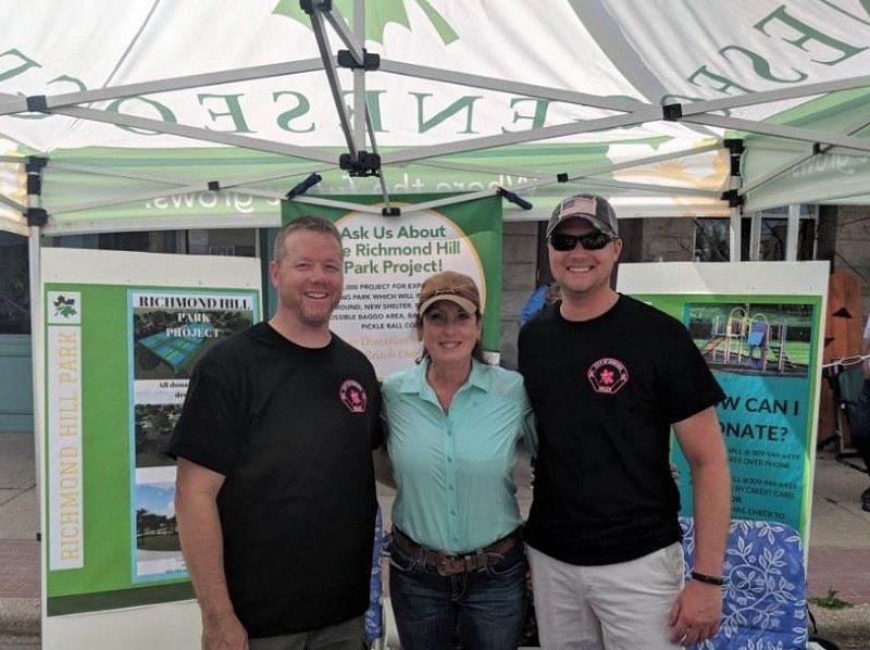 three smiling people under an event tent with posters behind them