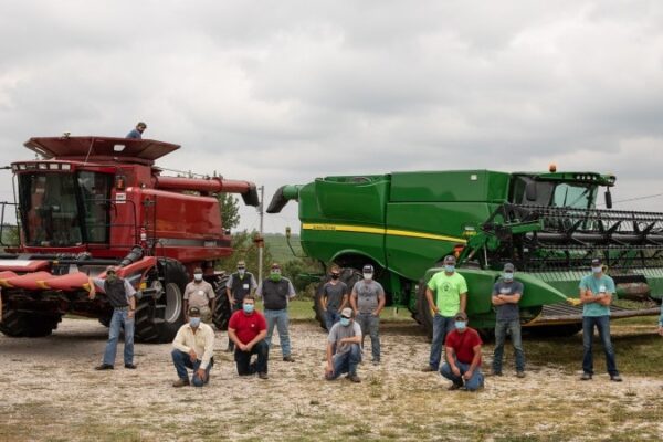 people in masks in front of farming equipment