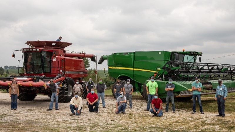 people in masks in front of farming equipment