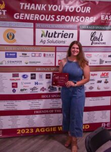 Carli Wright holding award and standing in front of event sponsorship banner