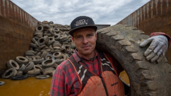 man holding a tire with a pile of tires in the background