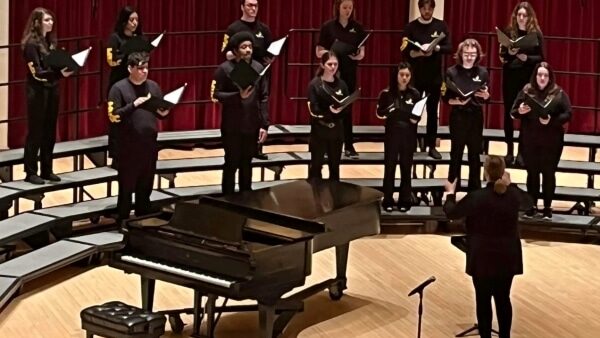 Choir director on stage with 12 choir members on risers singing