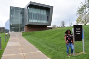 a student stands next to the Health Science Center sign