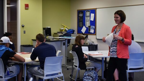 associate professor walking in a classroom with college students at their desks