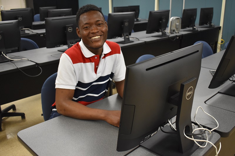 smiling male student sitting at a computer desk