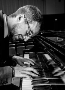 black & white image of smiling Corey Kendrick playing piano