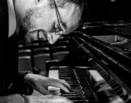 black & white image of smiling Corey Kendrick playing piano