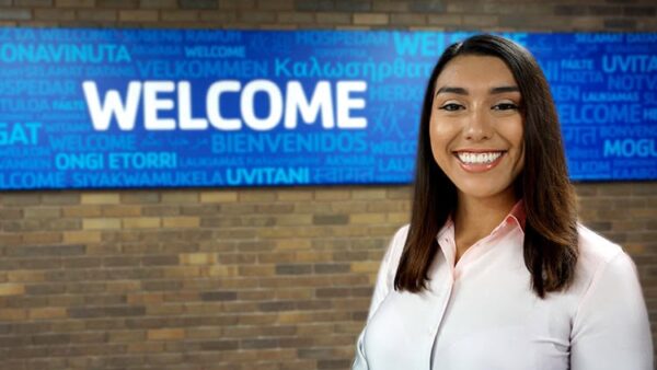 smiling woman in front of a sign that says welcome