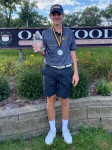 Dan O'Neill standing in front of Oakwood Country Club sign with award & medal