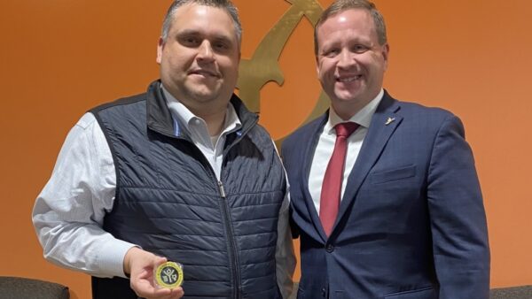 2 men smiling at camera with one holding excellence challenge coin