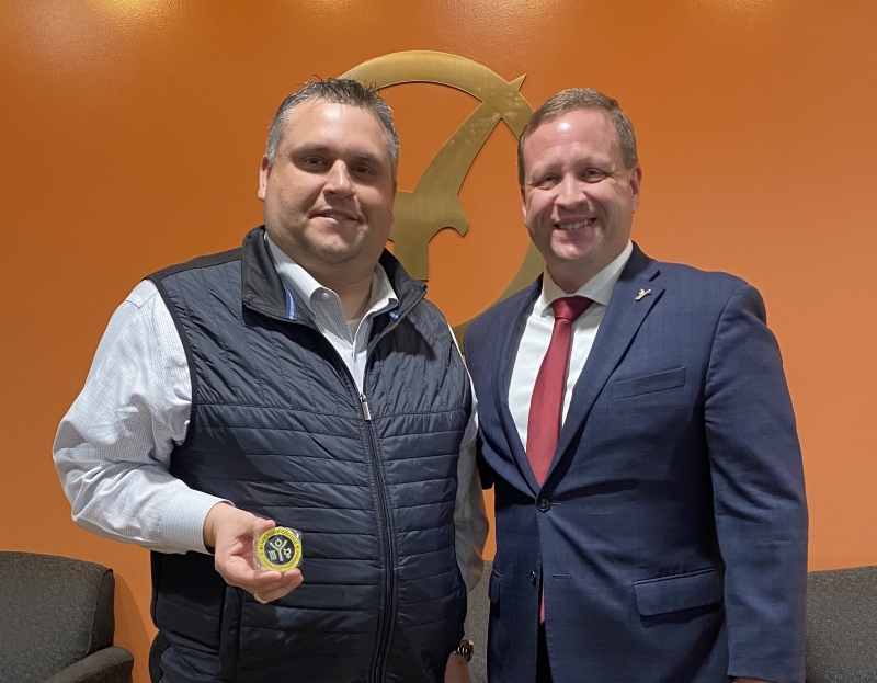 2 men smiling at camera with one holding excellence challenge coin