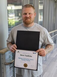 man smiling at camera and holding award certificate